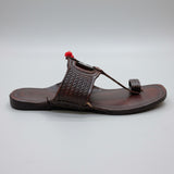 Brown sandal with a decorative strap on a light-colored floor