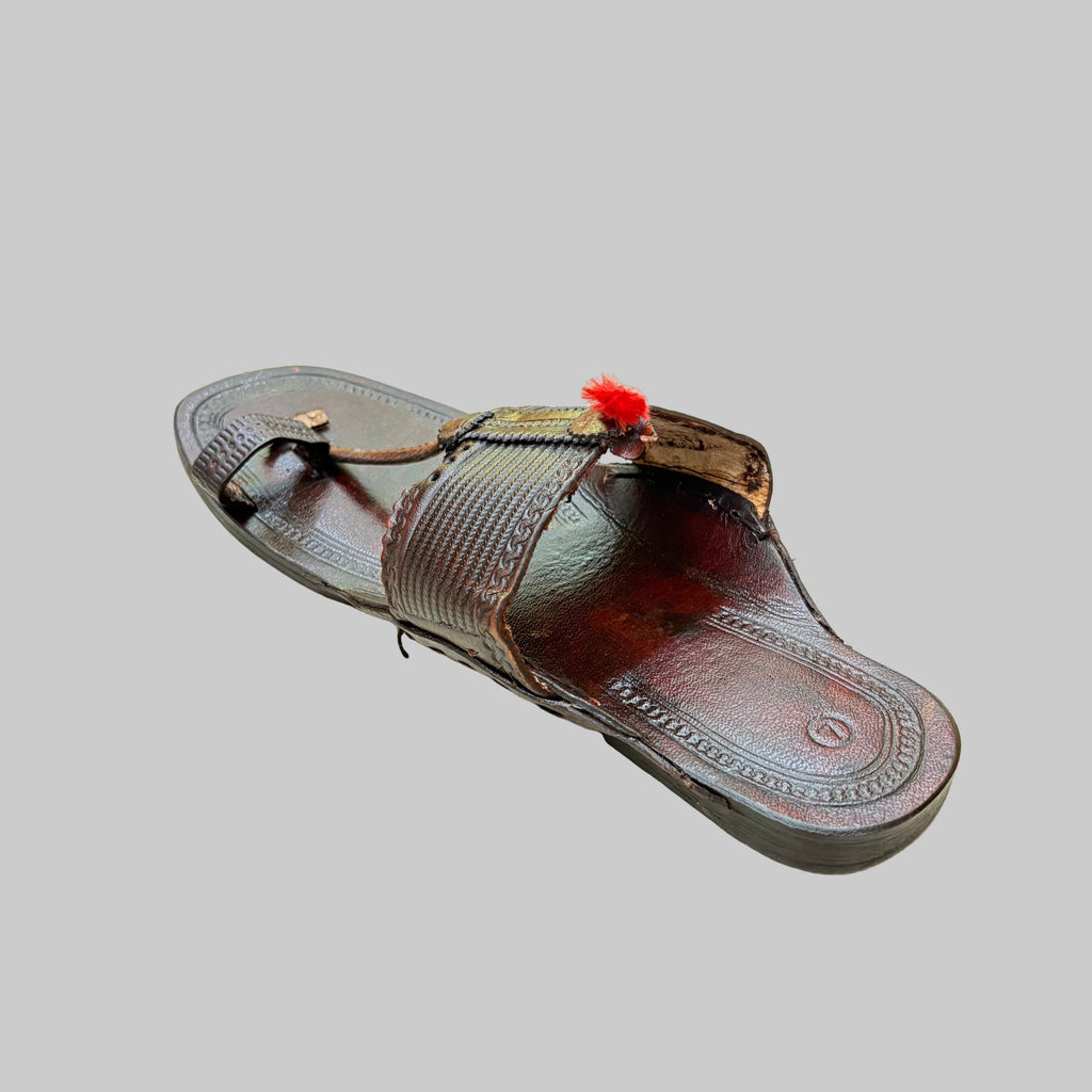 Brown sandal with decorative thong on a textured beige surface