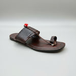 Brown sandal with decorative strap on a light marble surface