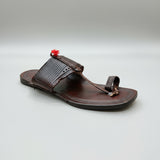 Brown sandal with decorative strap on a light marble surface