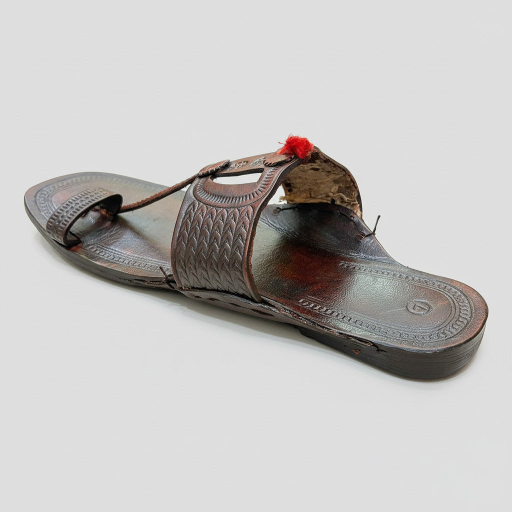 Brown sandal with intricate design on a beige textured surface