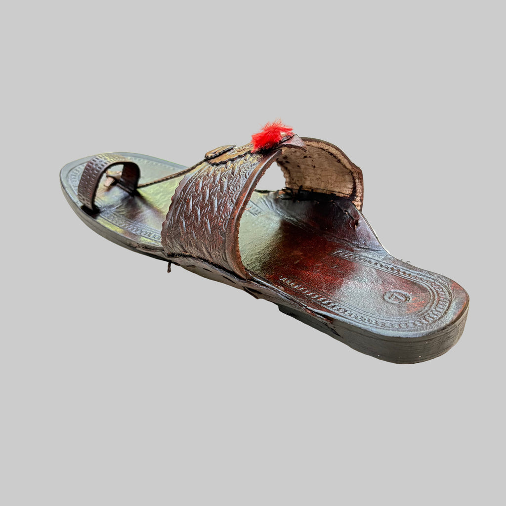 Brown sandal with a red decorative element on a light beige surface