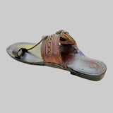Brown sandal with decorative straps on a light beige surface