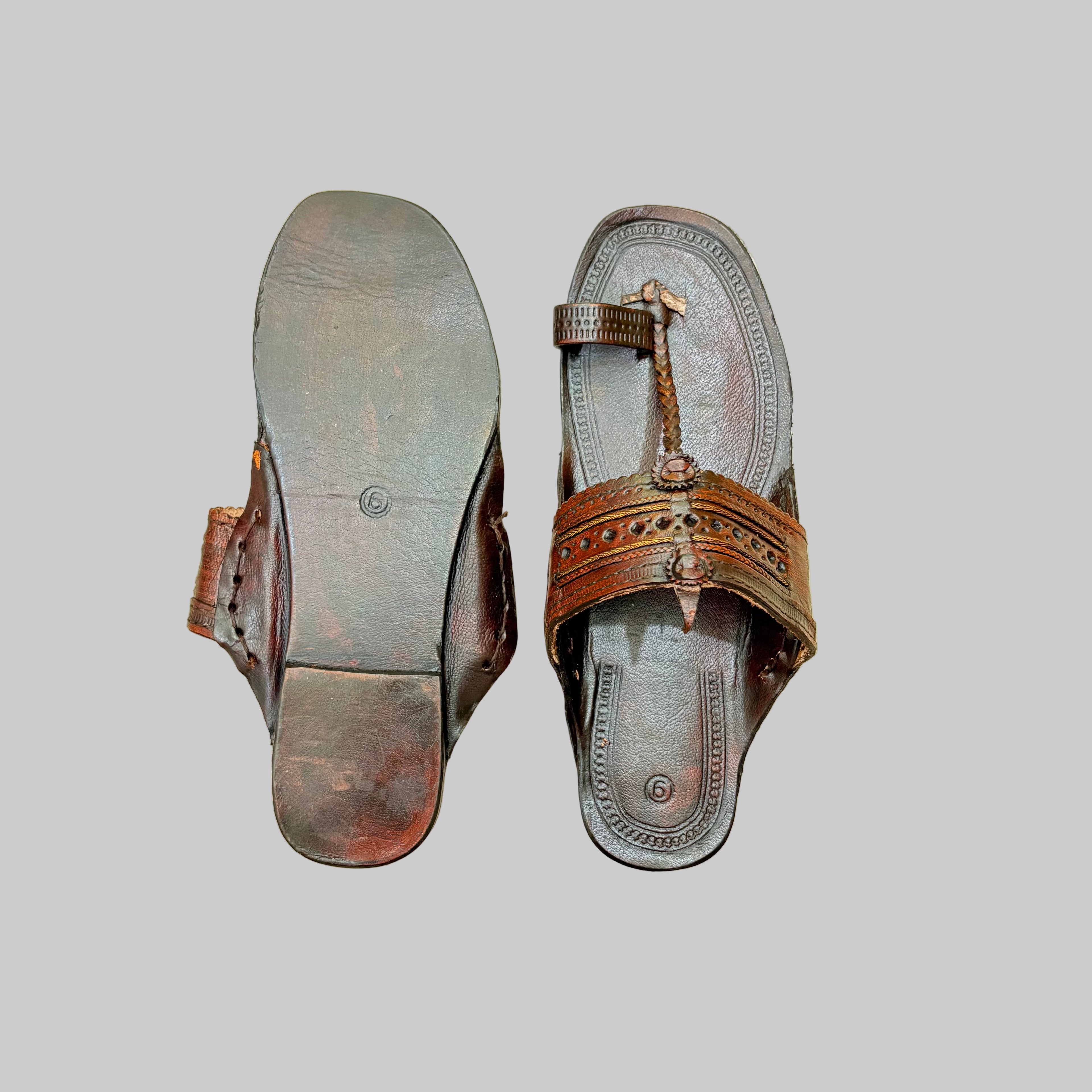 Pair of brown sandals with decorative straps on a beige textured background