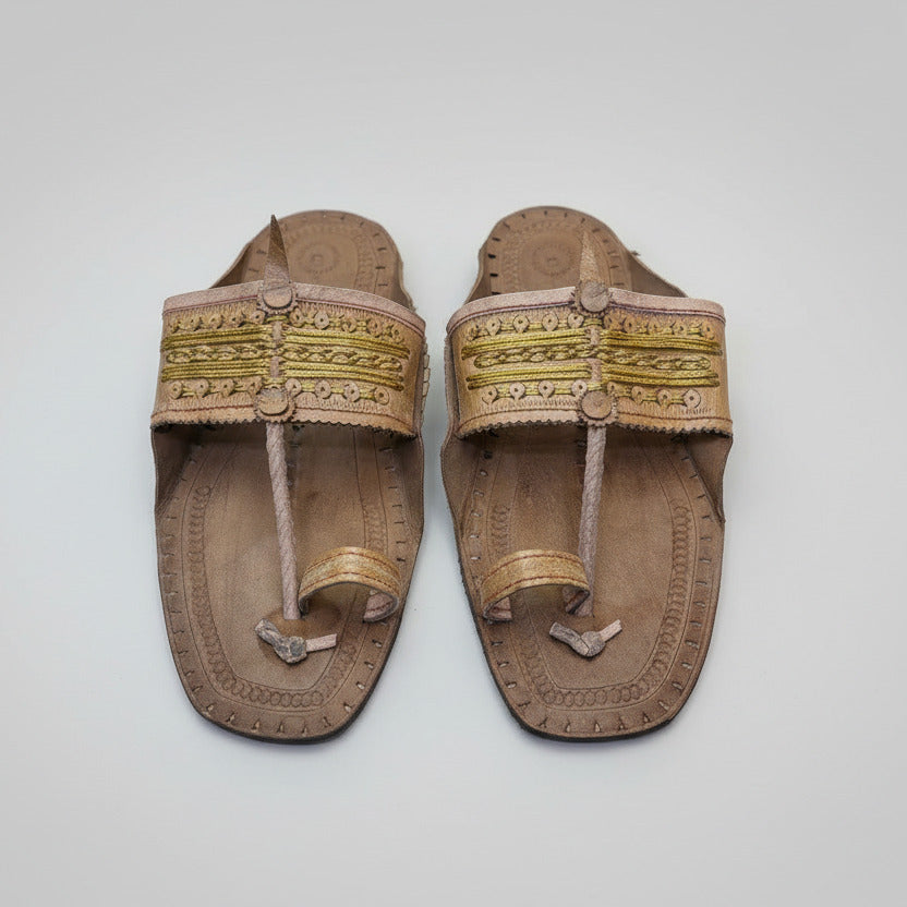 Pair of brown sandals with gold straps on a textured white surface