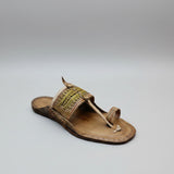 Brown sandal with decorative strap on a light gray floor