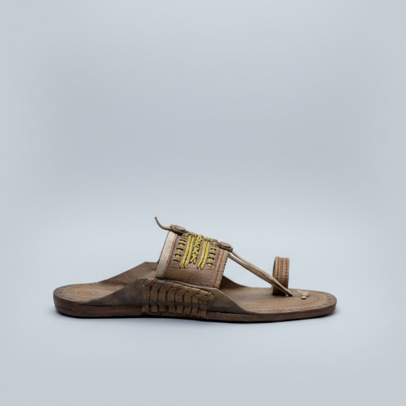 Brown sandal with decorative straps on a light-colored floor.