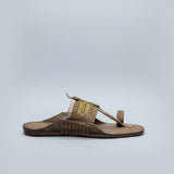 Brown sandal with decorative straps on a light-colored floor.