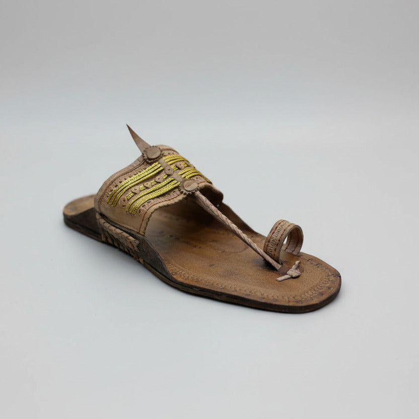 Brown sandal with yellow strap on a light gray floor