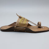 Brown sandal with decorative strap on a light gray floor