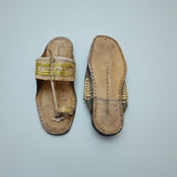 Pair of traditional sandals with decorative straps on a light blue textured background