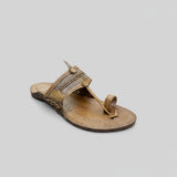 Brown sandal with decorative straps on a light gray surface