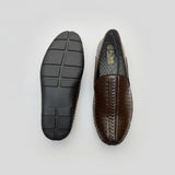Brown leather shoe with black sole on a beige textured surface