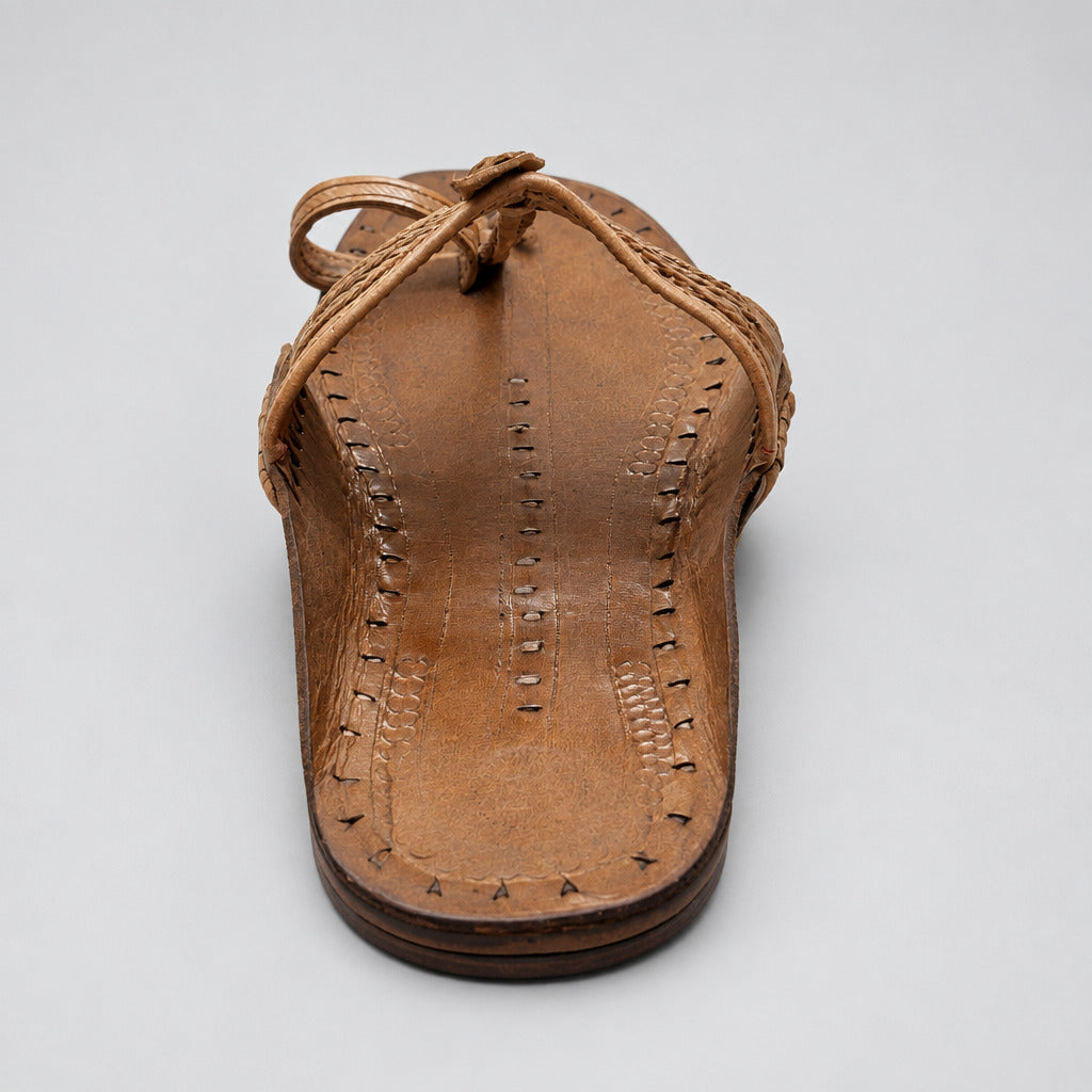 A single tan leather thong sandal with hand-stitched detailing, photographed from above on a light stone floor.