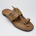 A single brown leather thong sandal with woven detailing and a pointed toe, resting on a polished beige marble floor.