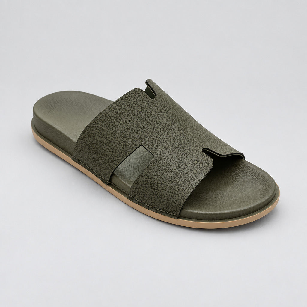 An olive green slide sandal with a textured strap and a light tan sole, resting on a polished beige marble floor.