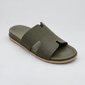 An olive green slide sandal with a textured strap and a light tan sole, resting on a polished beige marble floor.