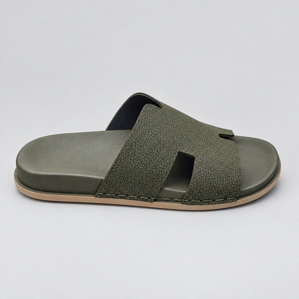 A single dark olive green slide sandal with a textured strap and a light tan outsole, resting on a beige marble floor.