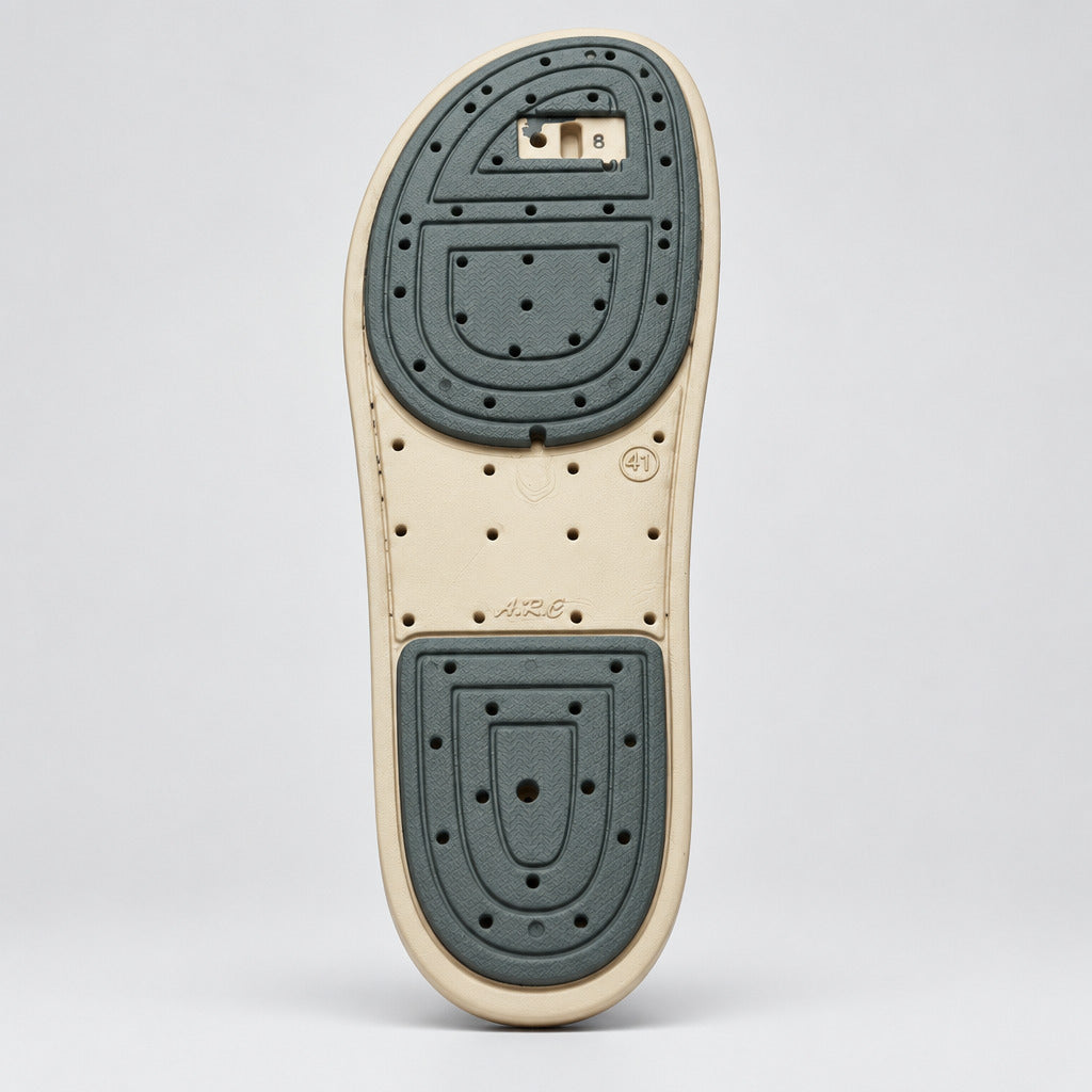The outsole of a shoe, showing a beige midsole with dark gray textured grip pads on the heel and toe, photographed on a light gray marble floor.