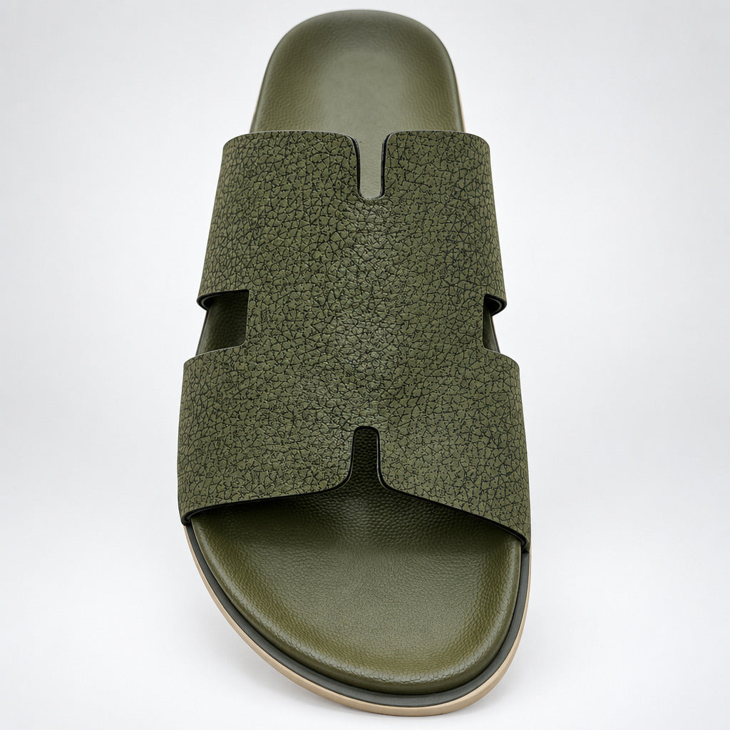 An olive green slide sandal with a textured pebbled strap and a matching contoured footbed, photographed from a top-down angle on a light beige marble floor.
