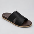 A single men's slide sandal with a wide black textured strap and a dark brown footbed, resting on a polished beige marble floor.