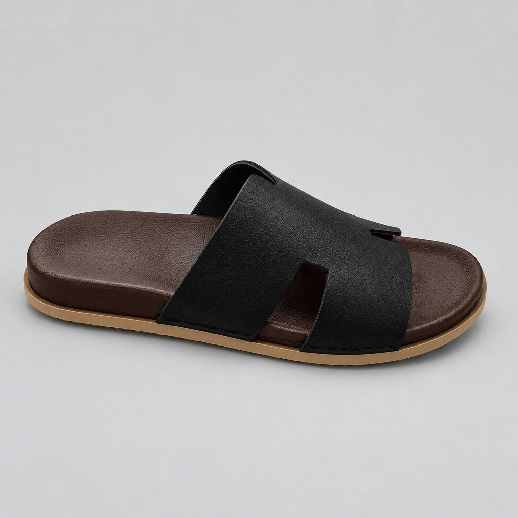 A single black slide sandal with a dark brown footbed and a light tan outsole, resting on a polished beige marble floor.