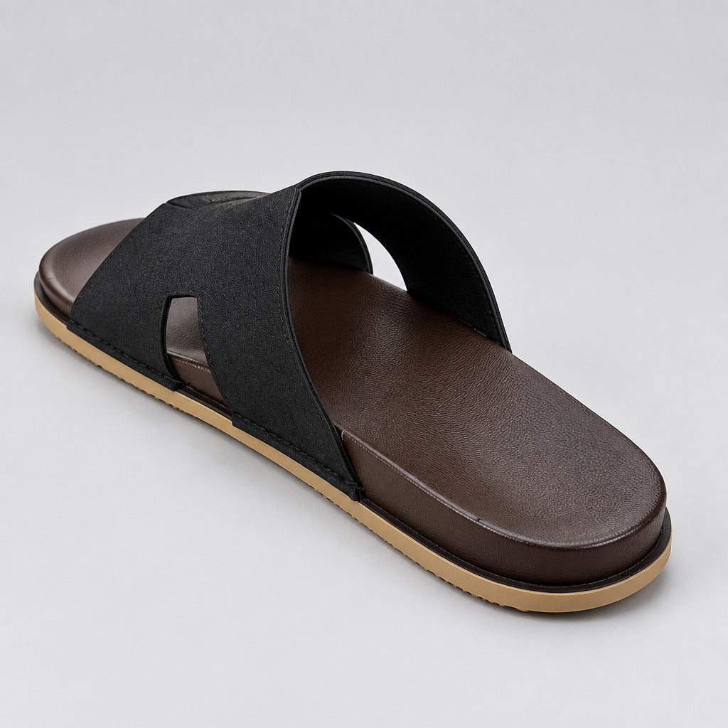 A single black slide sandal with a brown footbed and a beige outsole, photographed on a light beige marble floor.