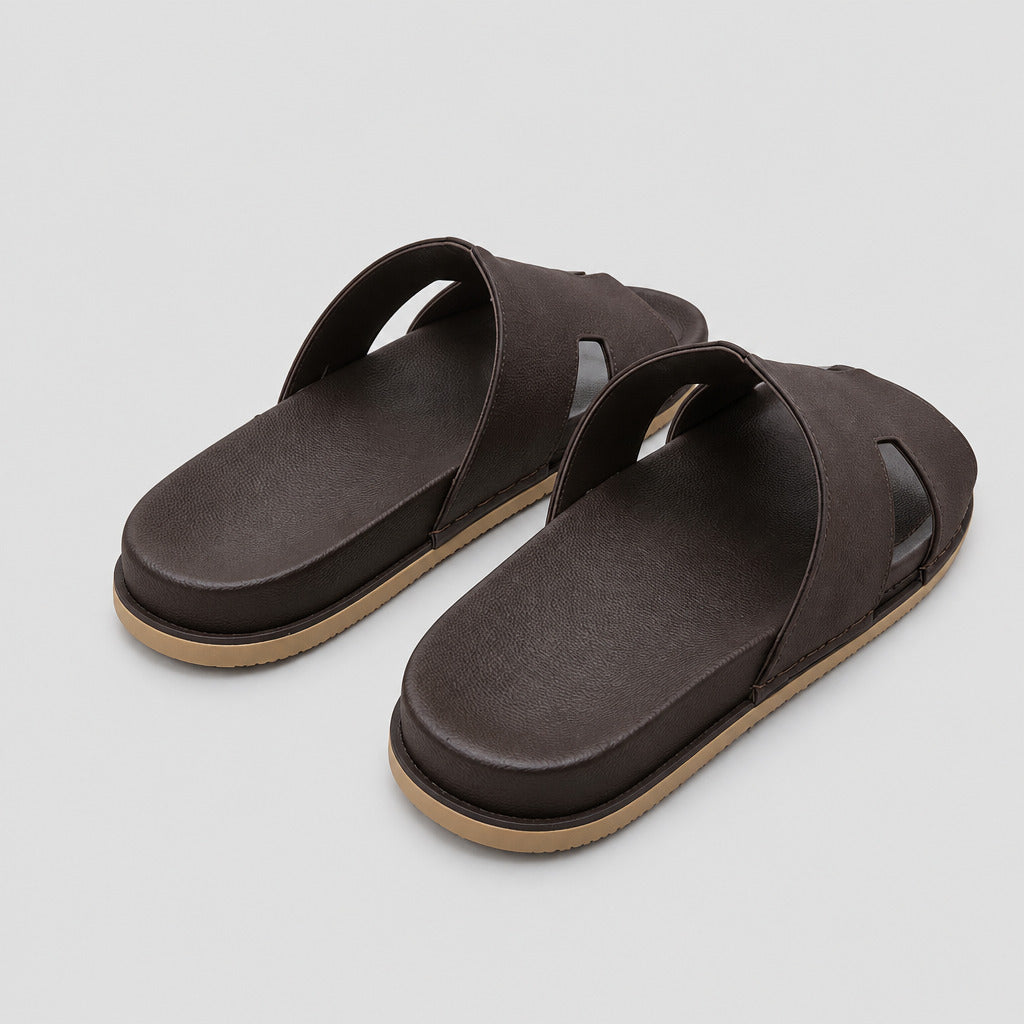 A pair of dark brown slide sandals with tan soles, placed on a polished beige stone floor.