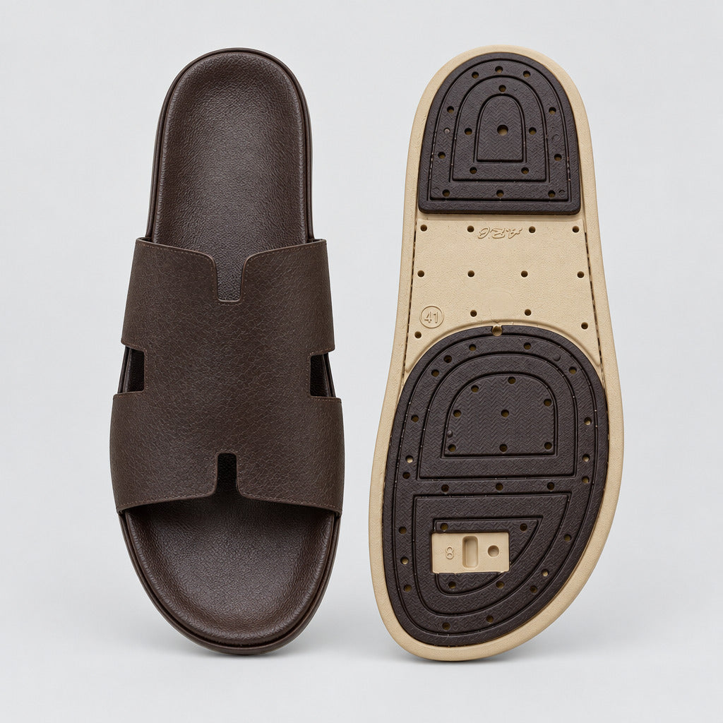 A pair of dark brown slide sandals shown on a light beige marble floor, with one sandal displaying its sole and the other showing the top view.